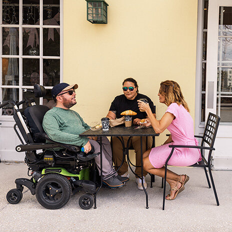 SMA advocate in wheelchair eating outside restaurant with two people