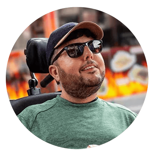 SMA Patient Advocate in wheelchair wearing sunglasses and hat with food truck in background